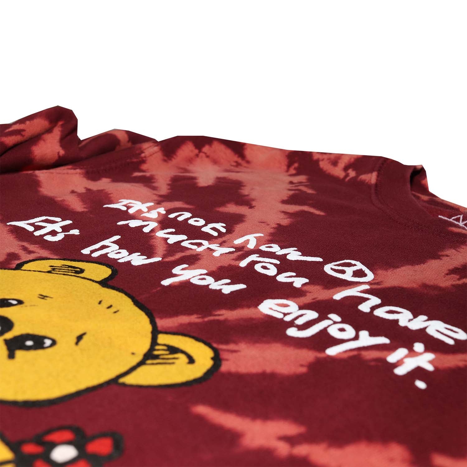 Front detail photo of puff ink text Teddy Bear sitting with mushrooms graphic printed on front of burgundy tie dye fleece fashion sweatshirt. Graphic includes bear, mushrooms, flower, peace sign and the text "It's not how much you have It's how you enjoy it".