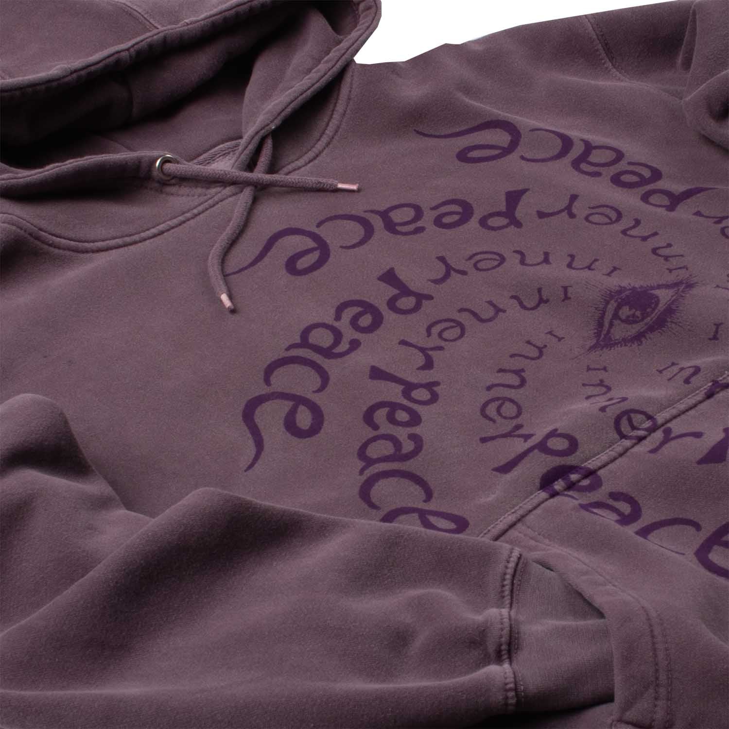 Closeup angled detail photo of many repetitions of "Inner Peace" text circling an "all seeing eye". Altru Inner Peace Dark Purple Hoodie. Garment dyed and washed for soft vintage look and feel,