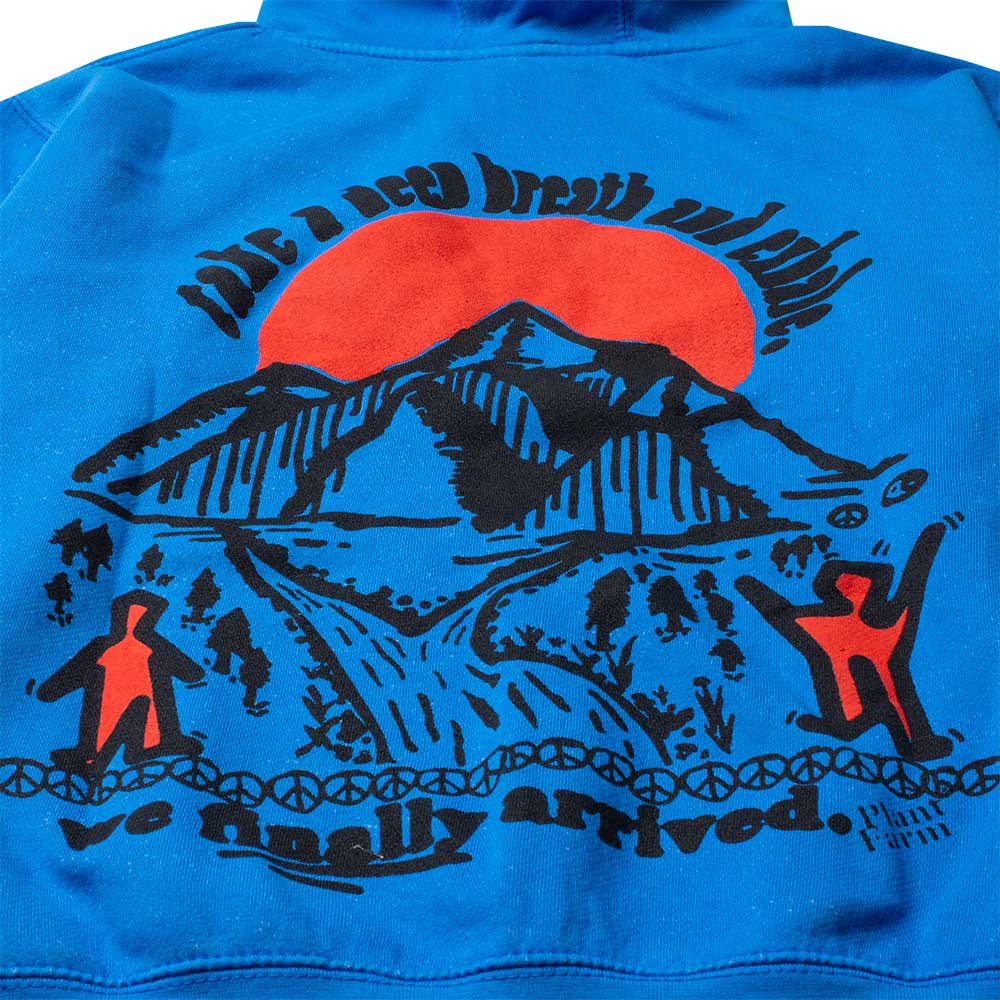 Close up photo of the back of blue hoodie graphic in red and black with the text take a deep breath and exhale, we finally arrived with a setting sun, peace signs, streams and happy people